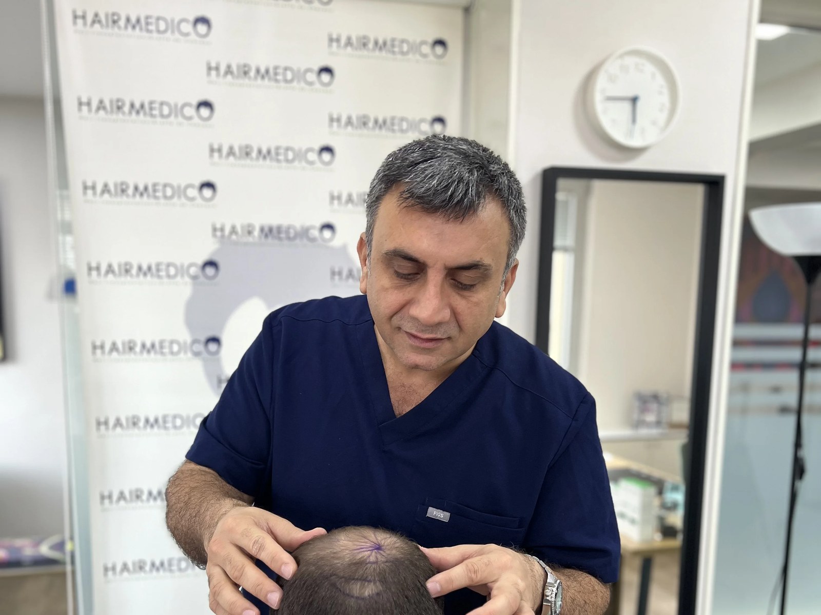 Dr. Arslan Musbeh examining a patient's scalp during consultation